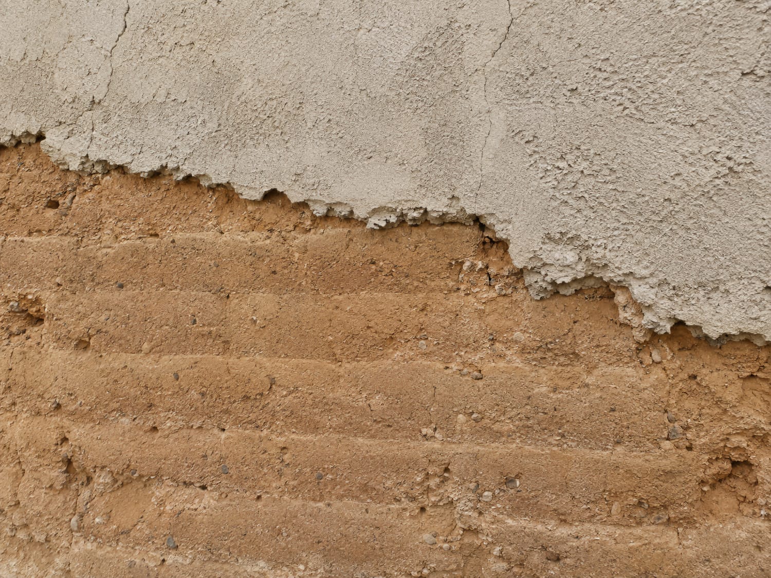 Mur en pisé partiellement recouvert d’un enduit, montrant la sensibilité du support à la gestion de l’humidité